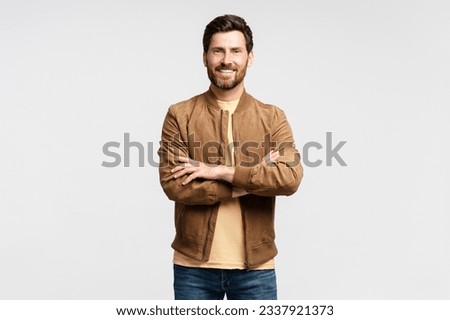 Handsome smiling bearded man wearing brown autumn jacket looking at camera isolated on grey background. Portrait of successful middle aged fashion model posing for pictures, studio shot 