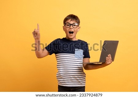 Excited inspired smart happy preteen boy wearing casual outfit, eyeglasses holding computer laptop isolated on yellow background, raising finger up showing eureka gesture, got creative idea solution Royalty-Free Stock Photo #2337924879