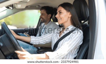 Cheerful confident pretty young woman sitting inside car with man instructor by her side, lady student holding hands on steering wheel, passing exams successfully at driving school, getting licence Royalty-Free Stock Photo #2337924981