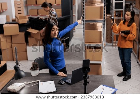 Logistics manager showing merchandise inventory and stock checking process while recording mobile phone video. Asian woman entrepreneur filming product promotion in storehouse