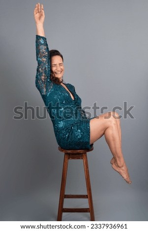 Studio portrait of beautiful mature woman balancing on a wooden stool. Cheerful and happy person. Isolated on gray background.