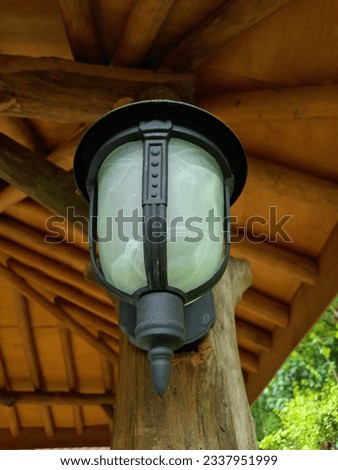 Antique and minimalist garden lamp with white mirror and black stalk attached to a wooden pole against a wooden ceiling background