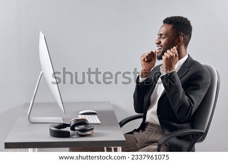 An African-American man sits at his desk in front of his laptop, wearing headphones and chatting on a video call, listening to music. The concept of student business training and online work.