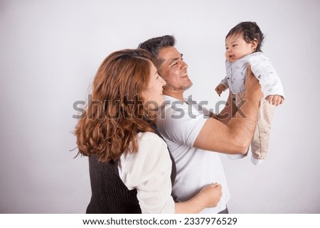 Beautiful photo of Dad and mom holding baby on light photo studio background. Family and baby concept.