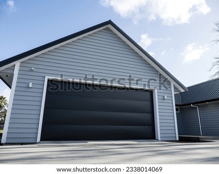 Double gray garage with black tilt-up retractable raised panel metal door and gable metal roof