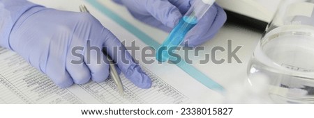 Scientist chemist checking composition of liquid in test tube in accordance with norms in table closeup. Concentration of toxic substances in detergents concept Royalty-Free Stock Photo #2338015827