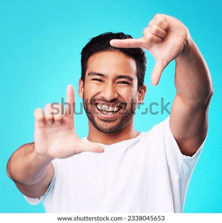 Happy, hand frame and portrait of a man for a selfie, creative aesthetic or advertising photography. Smile, laughing and face of an Asian person with a gesture for a photo on a blue background