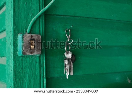 On the wall of a village house made of green planks, there is an old dirty switch, a bunch of keys to the locks hangs on a nail nearby. Selective focus.