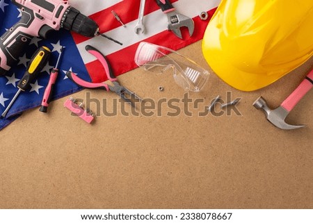 Embracing the spirit of female workers on Labor Day. Top view picture of an American flag and pink construction tools on wooden isolated background, providing space for adverts or text placement