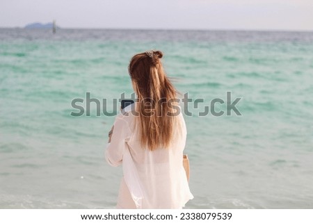 
A young woman wearing a white shirt was standing and looking at the vast and beautiful sea.