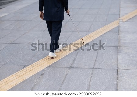 Close-up of the legs of a blind businesswoman walking along a tactile tile with a cane. 
