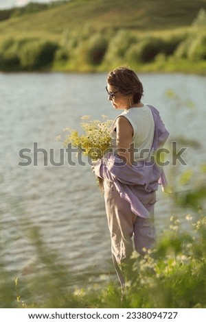 thoughtful, modern retiree immerses herself in the tranquility of a summer meadow, the wildflowers in her hands serving as a poignant reminder of life's continuous journey and her own resilience Royalty-Free Stock Photo #2338094727