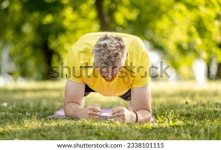 Man standing in plank position and practicing yoga outdoors at summer. Guy doing pilates workout for stretching muscles and abs stretght