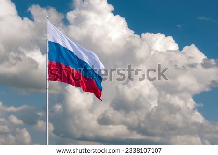 Waving the Russian flag against a blue sky with expressive white clouds on a summer day. State flag of the Russian Federation.