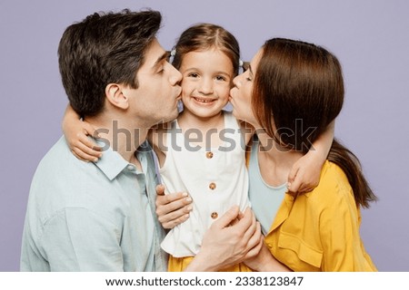 Side profile view young fun happy parents mom dad with child kid girl 6 years old wear blue yellow casual clothes hug daughter kiss look camera isolated on plain purple background. Family day concept