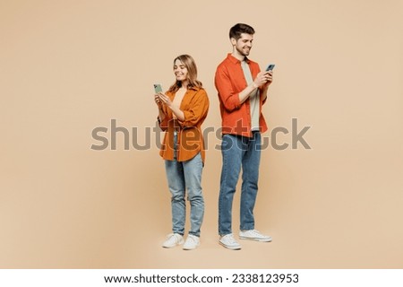 Full body side view fun young couple two friends family man woman wear casual clothes hold in hand use mobile cell phone together isolated on pastel plain light beige color background studio portrait