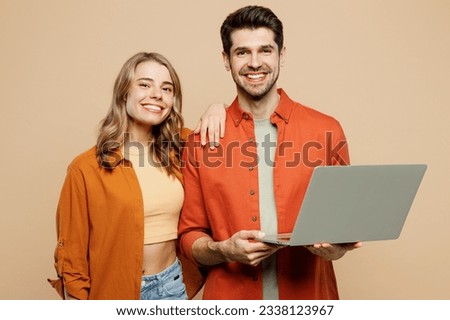 Young fun couple two friends family IT man woman wear casual clothes looking camera hold use work on laptop pc computer together isolated on pastel plain light beige color background studio portrait