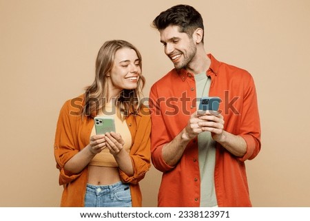 Young smiling happy satisfied couple two friends family man woman wear casual clothes hold in hand use mobile cell phone together isolated on pastel plain light beige color background studio portrait