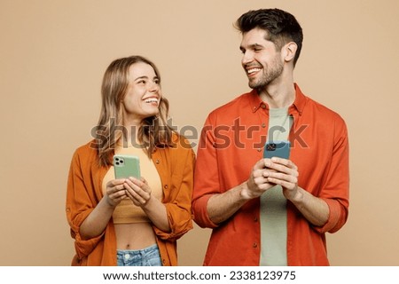 Young happy couple two friends family man woman wear casual clothes hold in hand use mobile cell phone together look to each other isolated on pastel plain light beige color background studio portrait