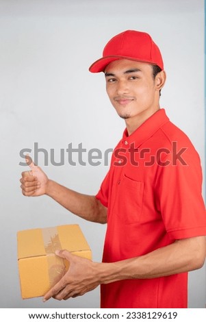Young man standing and holding a package box wearing red shirt and red hat isolated on white background