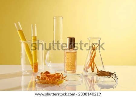 A serum bottle unbranded displayed on yellow background with some lab equipment containing cordyceps and essence. Space for design packaging. Front view, concept for rare chinese herbs Royalty-Free Stock Photo #2338140219