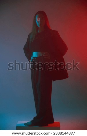 Studio portrait of a girl standing on a cube. She is dressed in a stylish black suit. Color photo. Vertical position of the frame. 