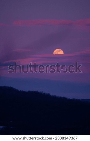 Mystical landscape with full moon rise in the cold season. The natural satellite of the earth observed at sunset among the colored clouds