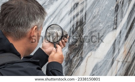 A person studies a mineral through a magnifying glass. The concept of the geologist's work. Background picture.