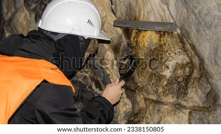 A woman in a mine examines a stone wall through a magnifying glass. The concept of the geologist's work. Background picture.