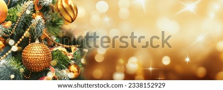 Christmas Tree With gold Baubles close-up against backdrop of golden sparkling Christmas lights. Wide format banner. Background with atmosphere of celebration and magic. Royalty-Free Stock Photo #2338152929