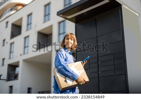 Young woman using smart phone while standing with a parcel delivered with post office machine with automatic lockers. New technologies in delivery service, self picking Royalty-Free Stock Photo #2338154849