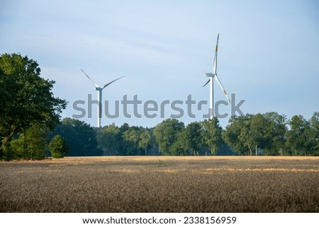 The picture shows a golden yellow grain field and in the background a wind turbine and green forests on a sunny summer morning in Germany.