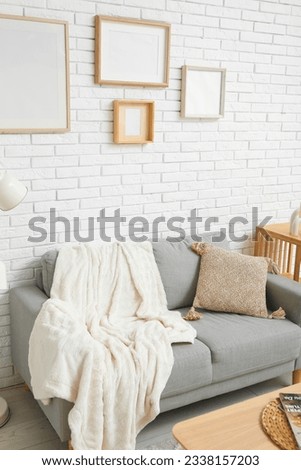 Interior of stylish living room with sofa and blank frames on white brick wall