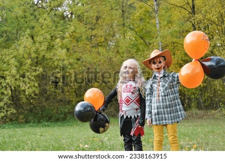 Two children girls girlfriends in Halloween costumes and makeup celebrate Halloween with black and orange balloons in their hands. Horizontal photo