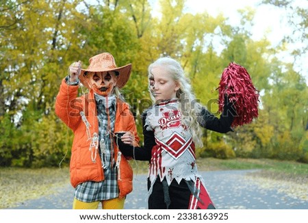 Girl child in an orange jacket and a cowboy hat shows her friend in a cheerleader costume her skeletons on a rope. Halloween celebration. Horizontal photo