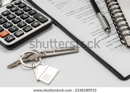 House key with "new homeowner" and calculator on office desk.
