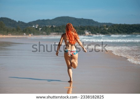 A beautiful girl runs along the beach and jumps into the waves. Sunny summer day. Girl with orange hair.