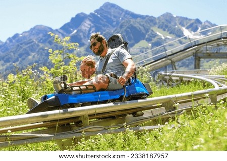 father and child having ride on summer toboggan called Rodelbahn rushing down the track. Beautiful mountains on background. Rosa Khutor resort, sochi, Russia
