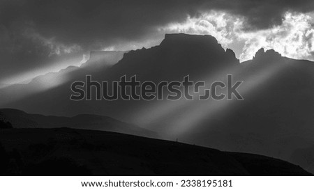 Black And White Mountain Silhouette Photograph With The Late Afternoon Sun Shining Through The Clouds And Through The Mountains In The Cathkin Park, Drakensberg, Region Of South Africa.