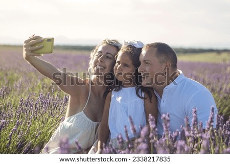 Young family with their daughter taking pictures with their mobile phone, in a beautiful lavender field. High quality photo