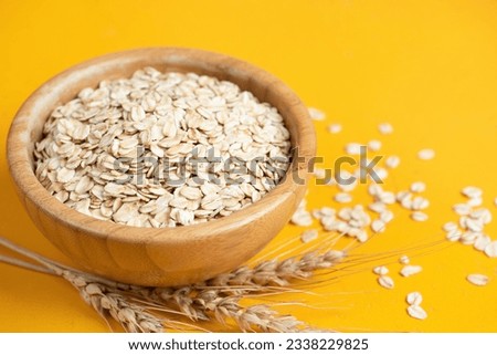 Rolled oats, oat flakes in wooden bowl on yellow background. Summer agriculture food harvest concept Royalty-Free Stock Photo #2338229825