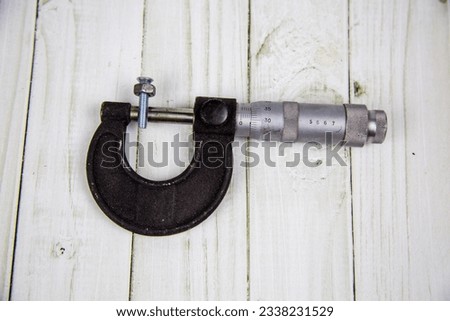 A metal micrometer with nuts and bolts on a gray wooden table. Tools, construction, production, design, structures.