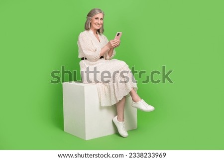 Full size photo of attractive old woman sit cube telephone typing wear trendy white clothes isolated on green color background