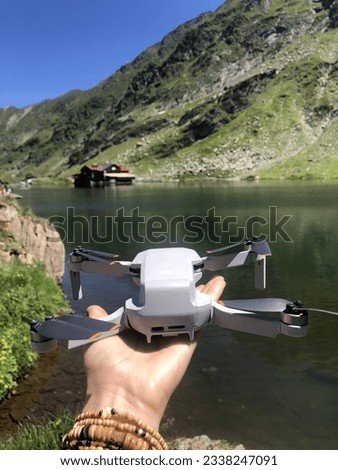 Drone lies on woman palm against of the lake and mountains. Hand holds compact drone on scenic landspace background. Vertical frame.