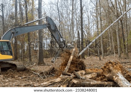 Excavator is being used by worker to clear land for house construction. Royalty-Free Stock Photo #2338248001