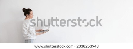 Young woman holding laptop, working. Millennial person in white sweatshirt on white background. People using technology. Horizontal banner, copy space right.