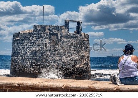 An iconic image of a senior woman fishing in front of the castle of san cristobal, Las Palmas.                               