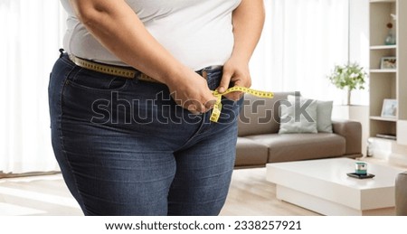 Obese woman wearing jeans and measuring waist in a room Royalty-Free Stock Photo #2338257921