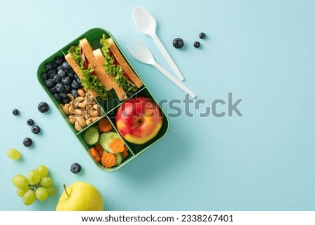 An appealing and health-conscious school lunch scene captured from above. The lunchbox features delectable sandwiches and fresh snacks on a blue background, offering copyspace for text or advertising Royalty-Free Stock Photo #2338267401