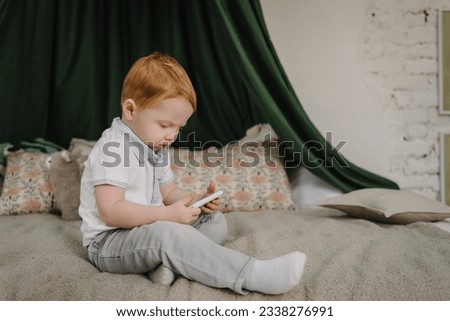 Cute little boy using smartphone, looking at screen. Child watching cartoons online on phone at home alone. Toddler playing mobile device video game. Kid gen Z using parental control app on cell phone